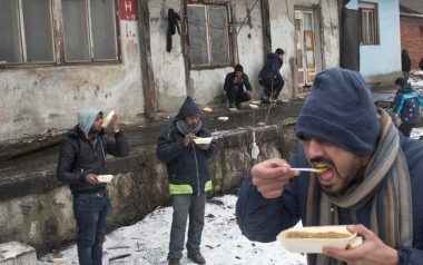 People eat meals outside an abandoned railway warehouse used as shelter by refugees in Belgrade, Serbia, Thursday, Jan. 5, 2017.